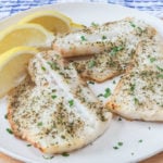 seasoned white fish fillets on white plate with lemon wedges