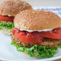 veggie burgers with buns and condiments on white plate