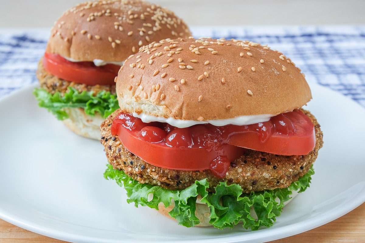 veggie burgers with buns and condiments on white plate