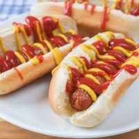 hot dogs in buns on white plate covered in ketchup and mustard