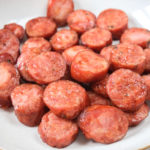 pieces of kielbasa on white plate on wooden board