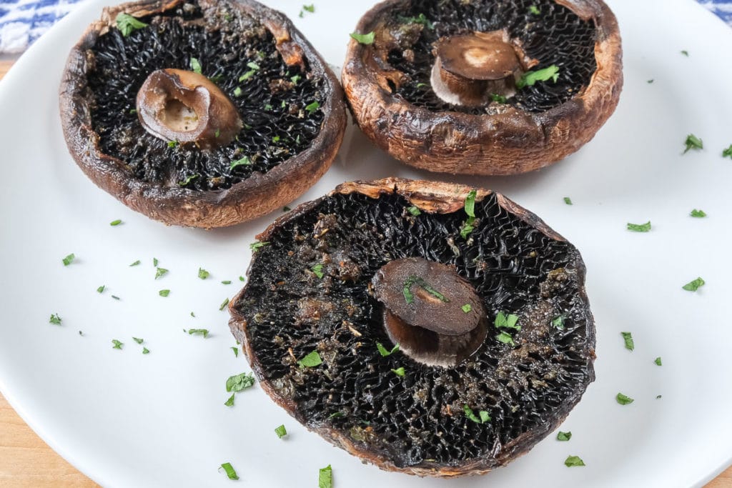 cooked portobello mushrooms on white plate with chopped parsley around