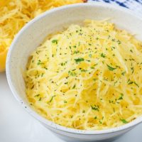 yellow spaghetti squash in bowl on plate with squash behind