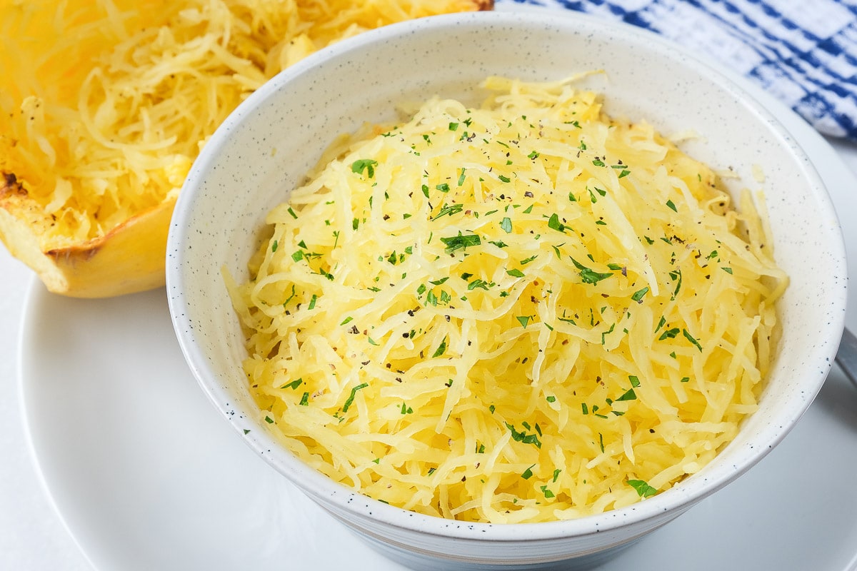 yellow spaghetti squash in bowl on plate with squash behind