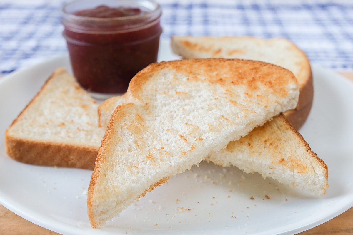 piece of toast on white plate with jam behind