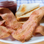 crispy turkey bacon on white plate with toast and jam behind