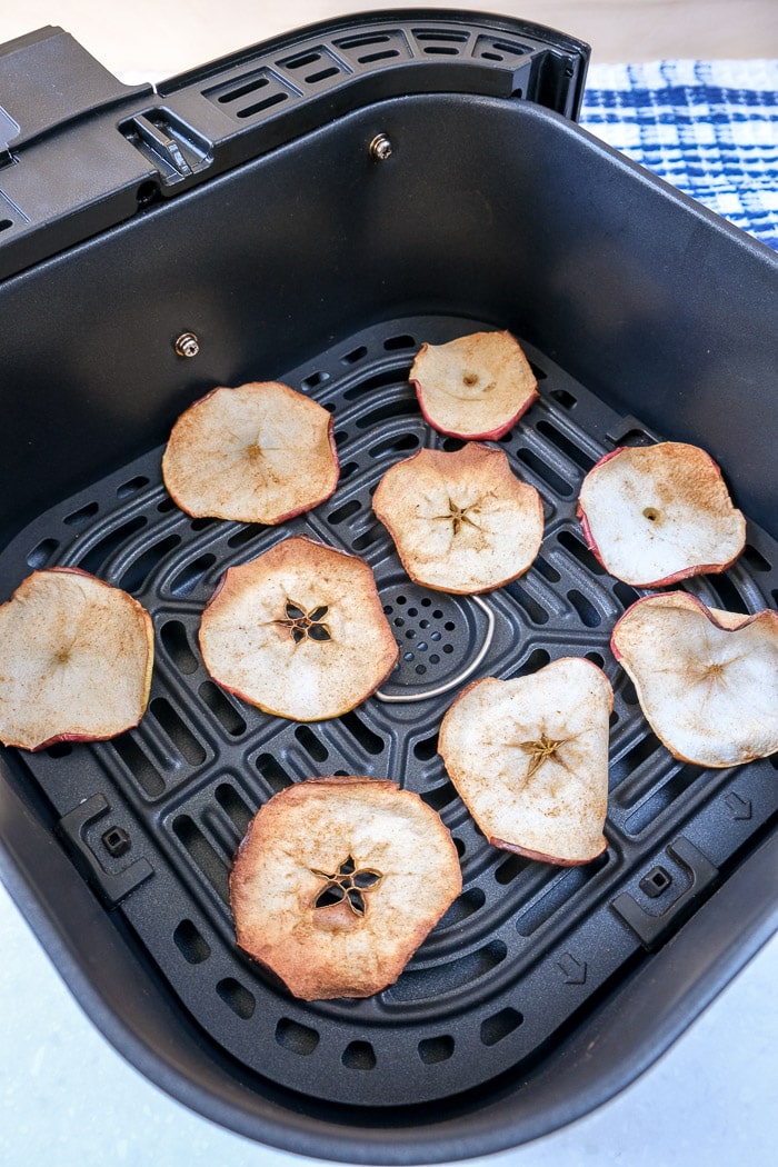 cooked apple chips in black air fryer tray laying on counter top