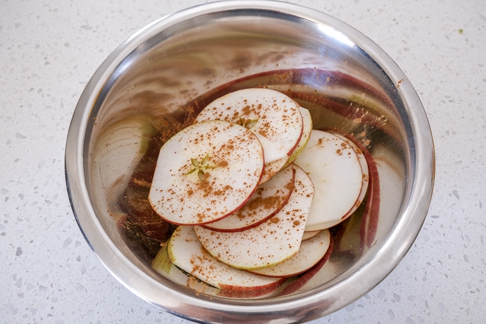 apple slices in metallic mixing bowl with cinnamon on top