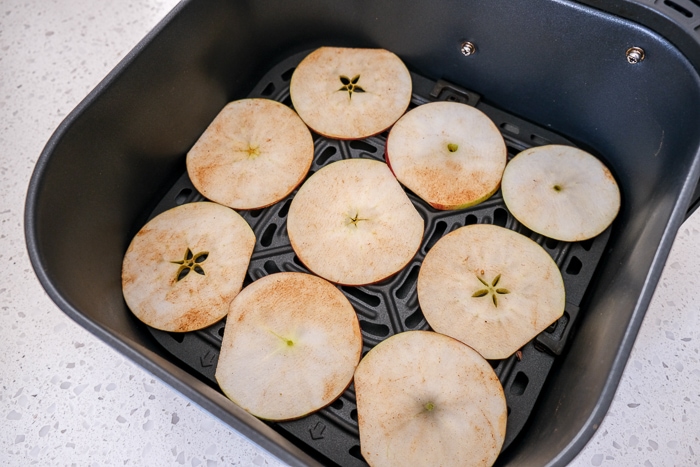 raw apple slices laying flat in black air fryer tray