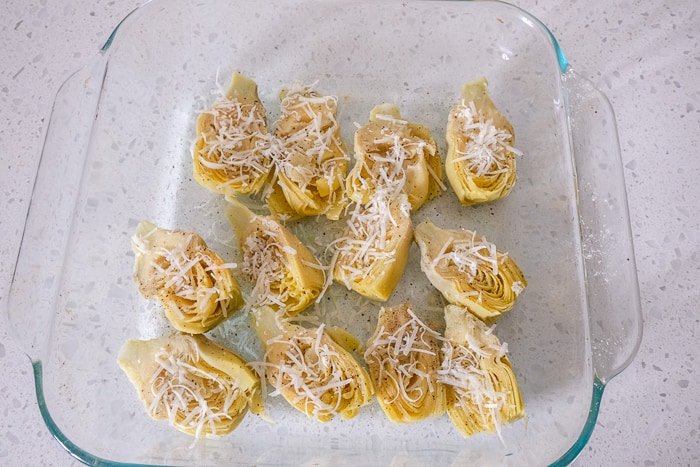 artichoke hearts in glass dish with parmesan cheese on top