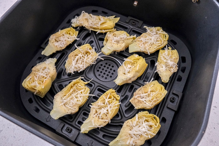 artichoke hearts in black air fryer tray on white counter top