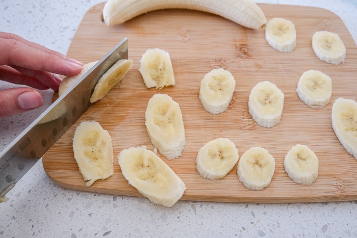knife slicing bananas on wooden cutting board on white counter