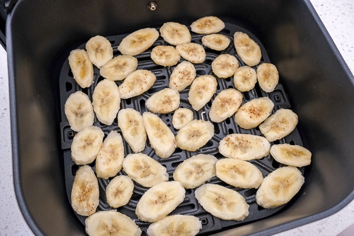 sliced bananas in black air fryer tray on white counter