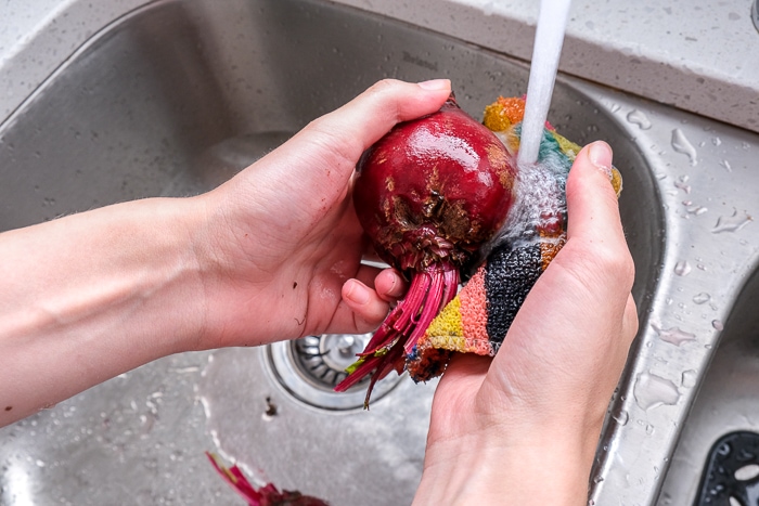 scrubbing beet with water and pad in metallic sink