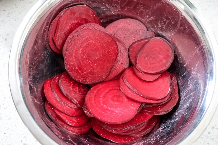 sliced beets with spices in silver mixing bowl on counter