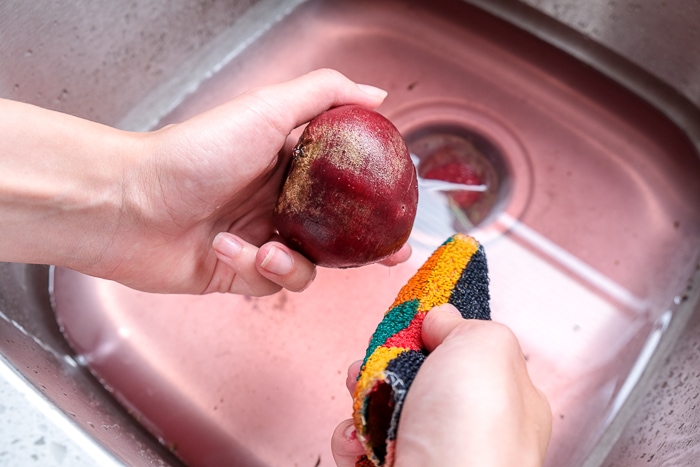 scrubbing beets off with scrubbing pad in metallic sink