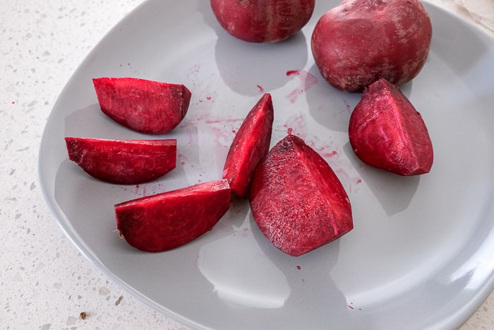 raw beets cut into wedges on grey plate on white counter