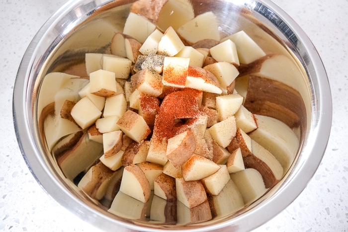 raw potato cubes in silver mixing bowl with oil and spices