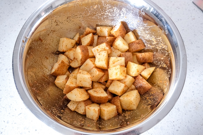 raw potato cubes in silver bowl covered in oil and spices