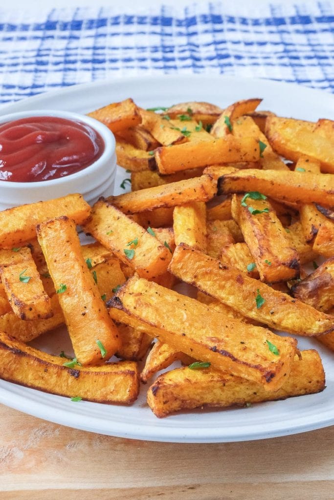 butternut squash fries on white plate on wood with ketchup beside
