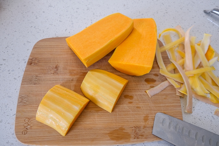 peeled butternut squash on wooden cutting board with knife beside
