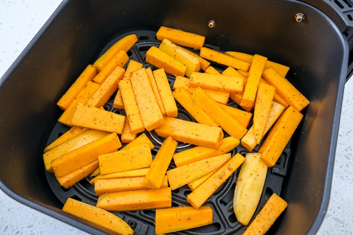 raw squash fries in black air fryer tray on white counter