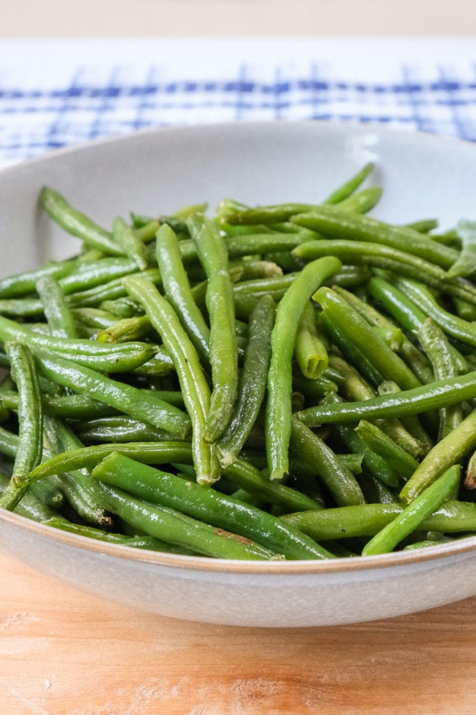 cooked green beans in bowl on wooden board