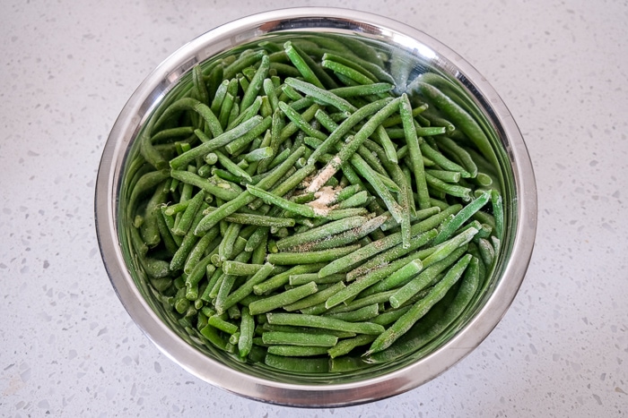 frozen green beans in silver mixing bowl with spices on top