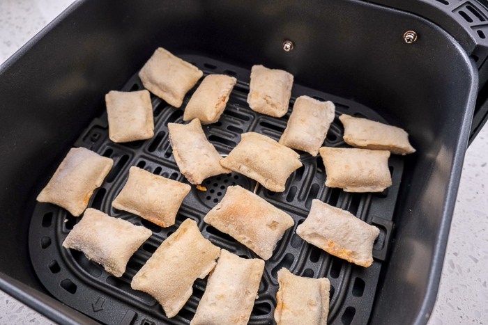 raw pizza rolls in black air fryer tray on white counter