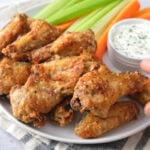 hand grabbing crispy garlic parm chicken wings from plate.