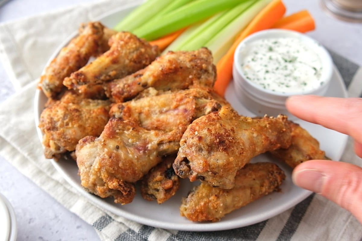 hand grabbing crispy garlic parm chicken wings from plate.
