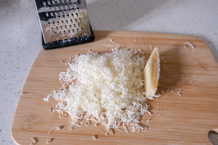 brick of parmesan on wooden cutting board on white counter
