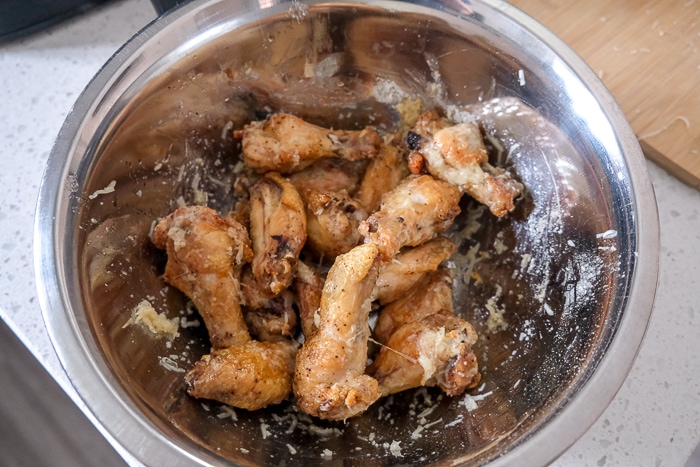 chicken wings in silver bowl mixed with parmesan cheese on white counter