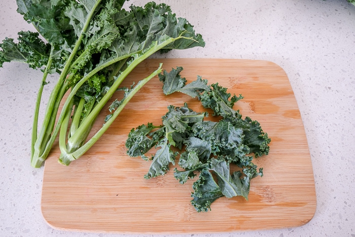 fresh kale ripped into pieces on wooden cutting board on counter