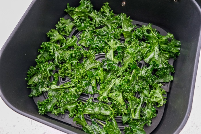 raw kale chips in black air fryer tray on white counter top