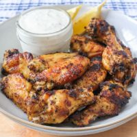 lemon pepper wings in bowl with dipping sauce on wooden board