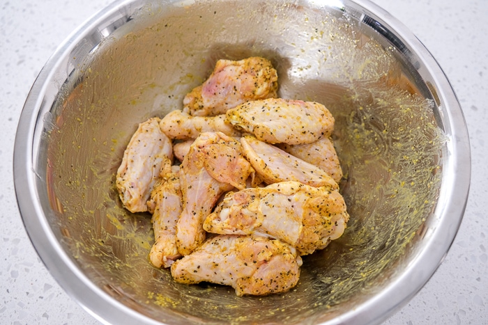 raw chicken wings in silver mixing bowl covered in yellow spice
