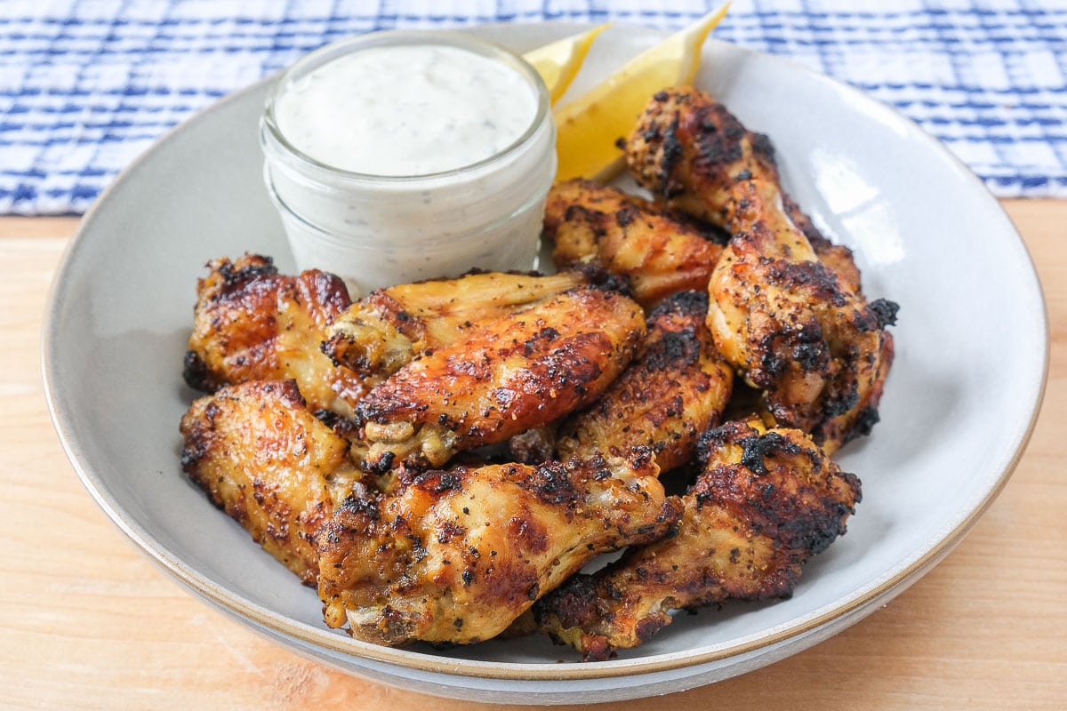 lemon pepper wings in bowl with dipping sauce on wooden board