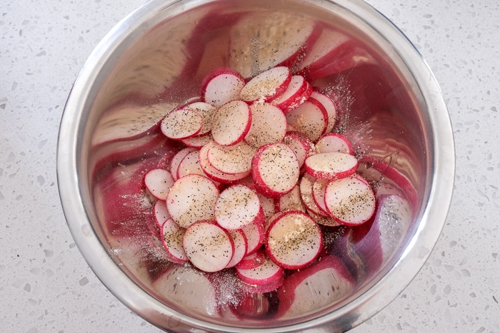 radish chips in silver mixing bowl with oil and spices on counter