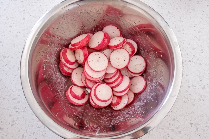 radish slices in spices in silver mixing bowl on white counter top