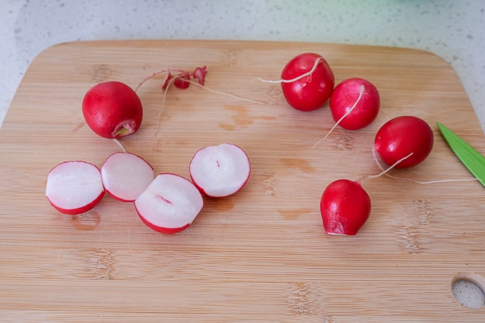 raw radishes on wooden cutting board on white counter