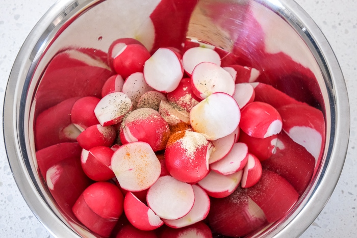 spices and oil on cut radishes in silver bowl