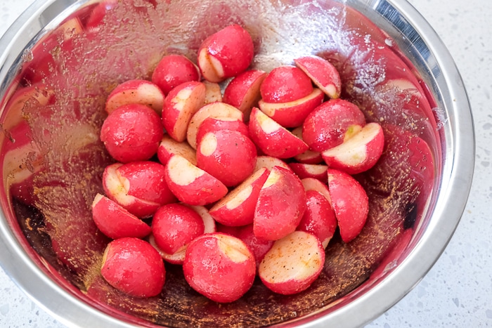 raw radishes covered in oil and spices in silver bowl on counter