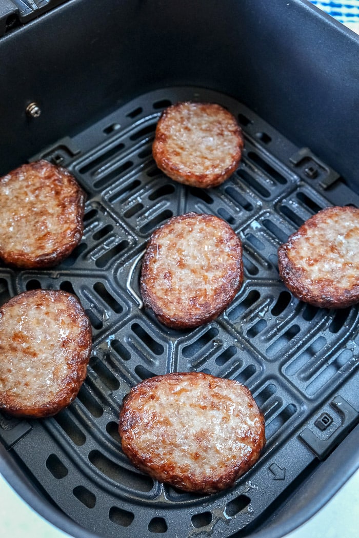 cooked sausage patties in black air fryer tray on white counter
