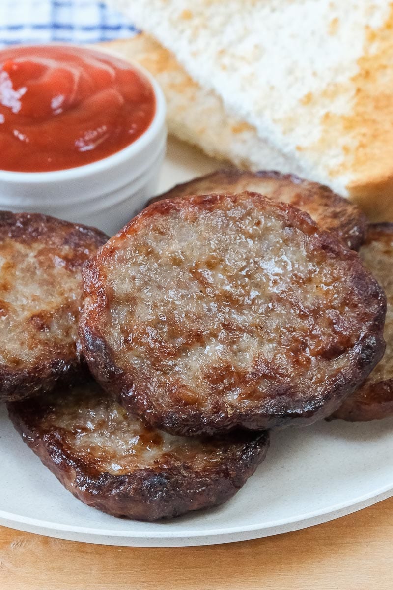 cooked sausage patties on plate with toast and ketchup behind