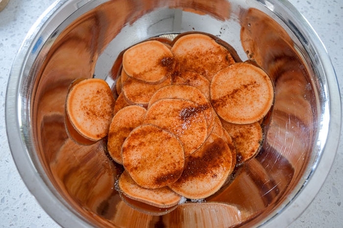 raw sweet potato slices in silver mixing bowl with spices on top