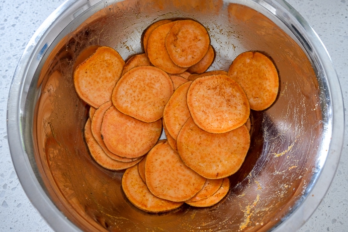 sweet potato slices mixed in spices in silver bowl