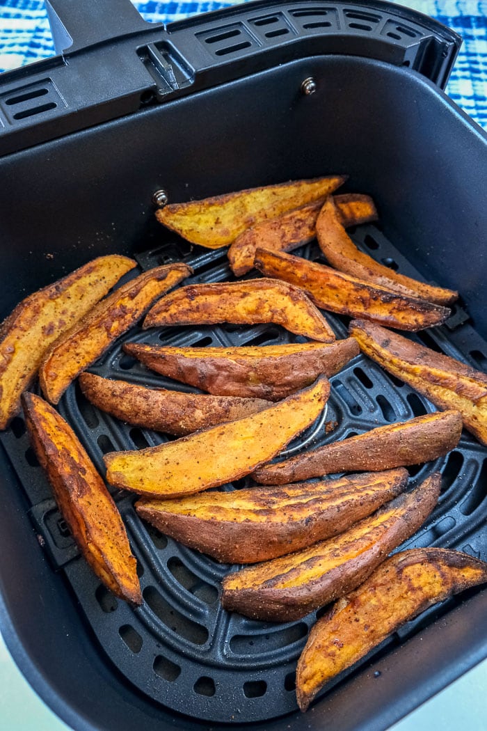 cooked sweet potato wedges in black air fryer tray on blue counter