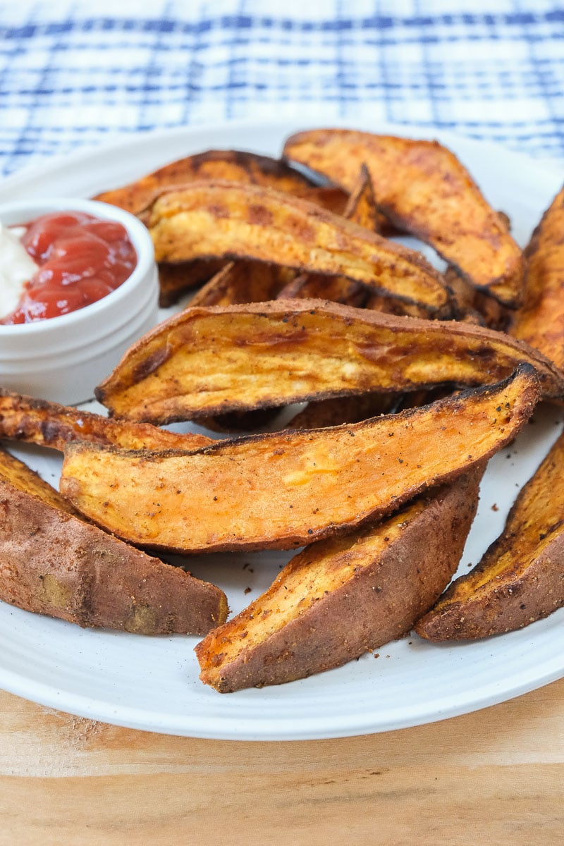 crispy sweet potato wedges on white plate with dipping sauce behind
