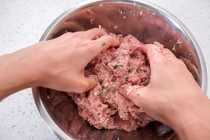 two hands in silver bowl mixing meat blend together on counter top